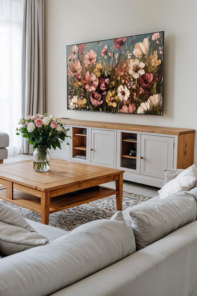 May include: A living room with a white sofa, a wooden coffee table, and a large floral painting hanging above a white cabinet. The painting features a variety of pink, yellow, and white flowers.