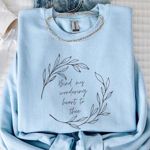 May include: Light blue sweatshirt with a floral wreath design and the text "Bind my wondering heart to thee".