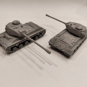 Op de afbeelding: Twee grijze speelgoed tanks, een met de toren naar voren gericht en de andere met de toren naar de zijkant gericht. Beide tanks hebben een gedetailleerd ontwerp en zijn gemaakt van plastic.