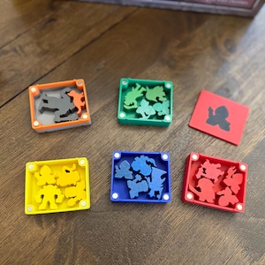 May include: A collection of colorful game pieces, including square tiles and small boxes with various shapes inside. The boxes are orange, green, yellow, blue, and red. The shapes are black, gray, and orange.