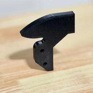 Puede incluir: Una pieza de plástico negro impresa en 3D con una parte superior curva y una base plana. La base tiene tres agujeros.