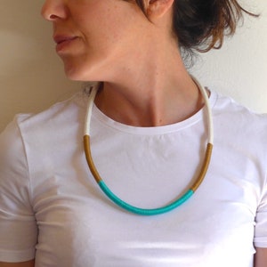 Könnte beinhalten: Eine türkisfarbene, weiße und goldene Seilkette. Die Kette besteht aus einem dicken Seil und wird von einer Person mit einem weißen Hemd getragen.