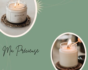 May include: Two candles in glass jars with lids. The candles are lit and the wax is a creamy white color. The text "HOMEMADE" is printed on the label of one candle. The text "Ma Précieuse" is written in cursive on a green background.