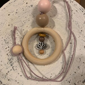 May include: A wooden teething ring with a pink, brown, and yellow bead necklace. The ring has a silver charm with a lotus flower design.