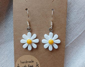 May include: A pair of silver daisy earrings with white petals and yellow centers. The earrings are on a brown card with the text "handmade with love" on a circle sticker.
