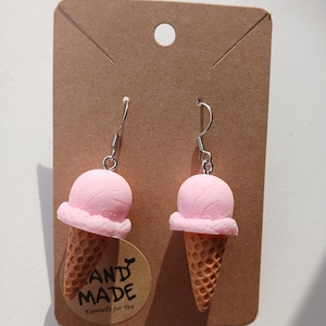 May include: A pair of dangle earrings featuring miniature pink ice cream scoops in waffle cones. The earrings are attached to a brown rectangular display card with a circular sticker that reads HAND MADE Especially for You.