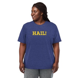 May include: A heathered blue short-sleeve t-shirt featuring the word HAIL! printed in bold yellow block letters across the chest. The garment has a crew neckline and a standard fit, constructed from a textured fabric with a subtle speckled appearance.