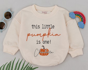May include: A cream colored long-sleeved onesie with the text "this little pumpkin is one!" and a small pumpkin with the name "Charlotte" underneath.