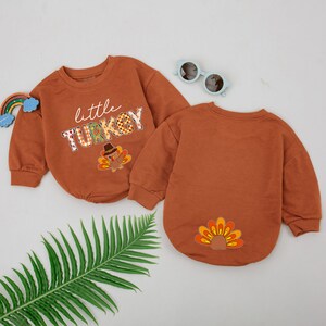 May include: Two brown long-sleeve shirts with a Thanksgiving theme. One shirt has the text "little TURKEY" with a turkey graphic. The other shirt has a turkey tail graphic.