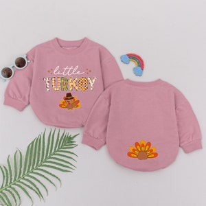 May include: Two pink long-sleeved shirts with a Thanksgiving theme. One shirt has the text "little TURKEY" with a cartoon turkey. The other shirt has a cartoon turkey tail.