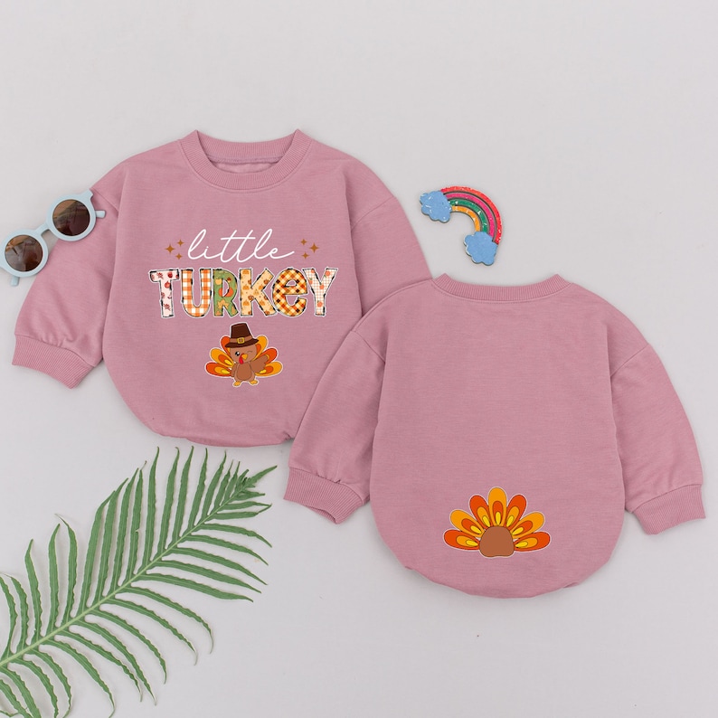 May include: Two pink long-sleeved shirts with a Thanksgiving theme. One shirt has the text "little TURKEY" with a cartoon turkey. The other shirt has a cartoon turkey tail.