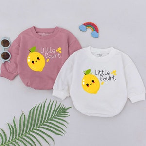 May include: Two long-sleeved shirts with a lemon graphic and the text "Little Squirt". One shirt is pink and the other is white.