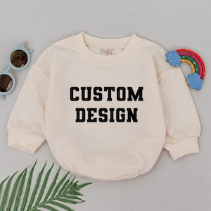May include: A cream colored sweatshirt with the text "CUSTOM DESIGN" printed in black on the front.
