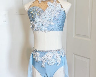May include: A light blue dance costume with a halter top and a skirt. The top and skirt are decorated with white lace and rhinestones. The skirt has a sheer overlay.