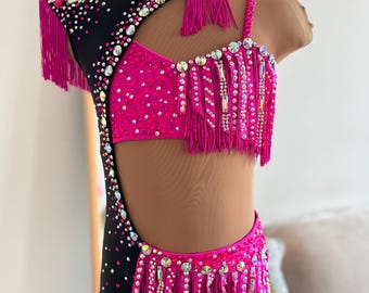 Puede incluir: Un vibrante disfraz de baile con una combinación de colores negro y rosa intenso. El maillot está adornado con pedrería y flecos, con un tocado a juego. El disfraz está diseñado con un corte en el lateral y se exhibe en un maniquí.