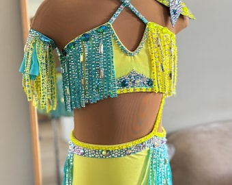 Op de afbeelding: Een oogverblindend danskostuum in geel en blauwgroen, versierd met sprankelende strass-steentjes en franjes. De set bevat een choker, een schouderstuk en een turnpakje met bijpassende versieringen. Het kostuum wordt op een mannequin getoond.