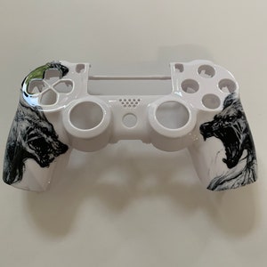 May include: White PlayStation 4 controller with a black and white wolf design on the front and back. The controller has a green button on the front.