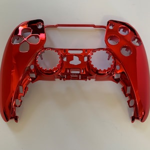 May include: A red plastic shell for a video game controller. The shell has a glossy finish and is designed to fit a standard controller.