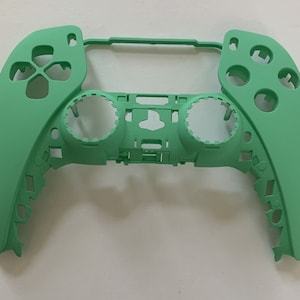May include: A green plastic shell for a video game controller. The shell has cutouts for buttons, joysticks, and triggers.