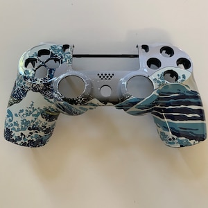 May include: A white and blue PlayStation 4 controller with a Great Wave off Kanagawa design.