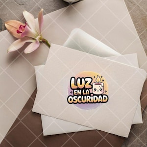 May include: A white card with a colorful sticker featuring a cartoon candle with a smiling face. The text on the sticker reads "Luz en la Oscuridad" which translates to "Light in the Darkness".