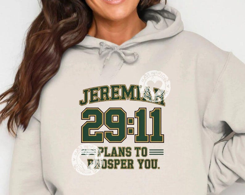 Może przedstawiać: Jasnobeżowa bluza z kapturem z napisem "JEREMIAH 29:11 PLANS TO PROSPER YOU" w zielonych i złotych literach. Bluza ma sznurek i przednią kieszeń.