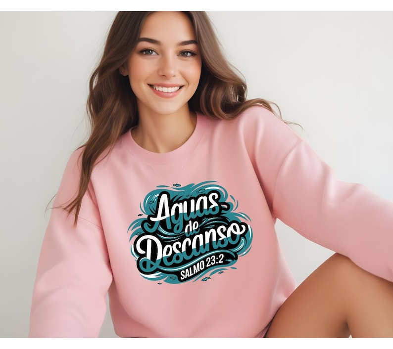 May include: Pink sweatshirt with a teal blue graphic design that says "Aguas de Descanso" with the text "Salmo 23:2" underneath.