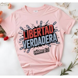 May include: Pink t-shirt with a graphic design that says "LIBERTAD VERDADERA" in red and black letters with a chain design around the words. The text "G&aacute;latas 5:1" is printed below the graphic.