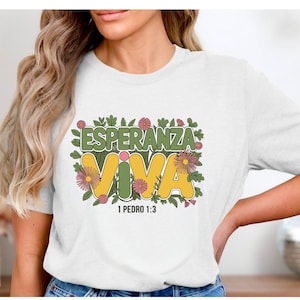 May include: White t-shirt with a green, yellow, and pink floral design. The text "Esperanza Viva" is in yellow with a green outline. The text "1 Pedro 1:3" is below the design.