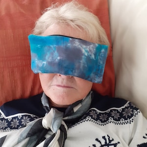 Könnte beinhalten: Eine Person trägt einen weißen Pullover mit einem blauen und weißen Rentier-Design, eine blaue und graue Augenmaske und einen blauen und weißen Schal.