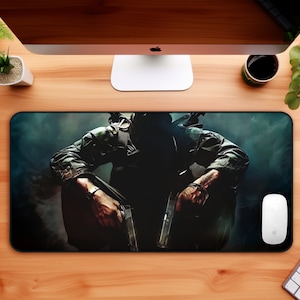 May include: A black and green gaming mouse pad with a dark, shadowy image of a person holding two guns. The person is wearing a black tactical vest and camouflage clothing.