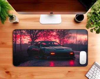 Puede incluir: Alfombrilla de ratón negra con ilustración de coche deportivo. El coche oscuro tiene luces rojas sobre un fondo de puesta de sol. Un ratón y teclado blancos están sobre un escritorio de madera.