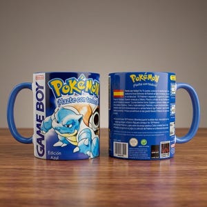 Puede incluir: Dos tazas de cerámica azules con el logo de Pokémon y un gráfico de Blastoise. Las tazas tienen asas azules y el texto "Game Boy" y "Edición Azul". Están sobre una superficie de madera.