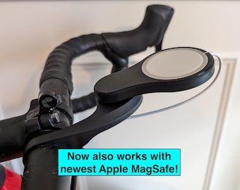 May include: Black bicycle handlebar with a mounted black and white device. The device has a circular white centre and is connected by a white cable. Text in a blue box reads "Now also works with newest Apple MagSafe!"