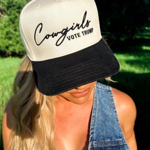 K&ouml;nnte beinhalten: Eine wei&szlig;e und schwarze Baseballkappe mit dem Text "Cowgirls Vote Trump" in schwarzer Stickerei.