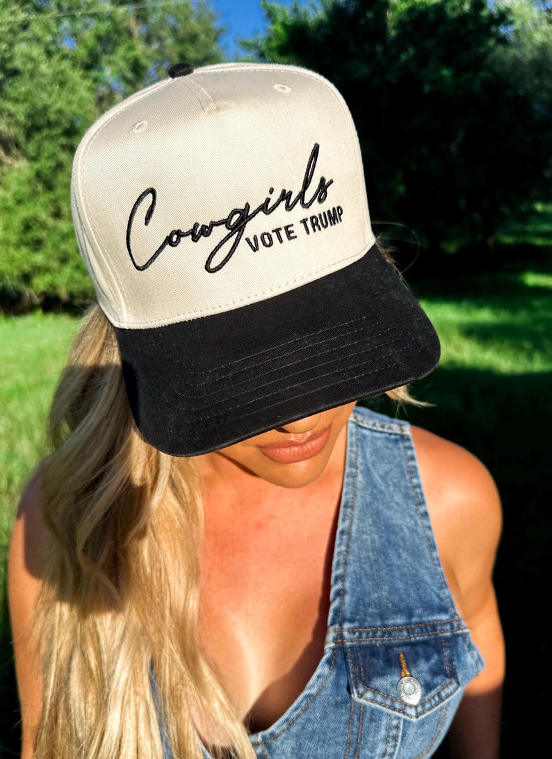 K&ouml;nnte beinhalten: Eine wei&szlig;e und schwarze Baseballkappe mit dem Text "Cowgirls Vote Trump" in schwarzer Stickerei.