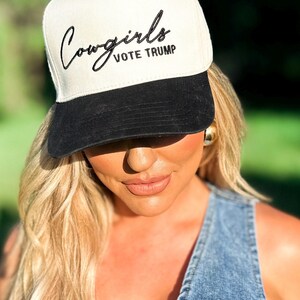 K&ouml;nnte beinhalten: Eine wei&szlig;e und schwarze Baseballkappe mit dem Text "Cowgirls Vote Trump" in schwarzer Stickerei auf der Vorderseite.