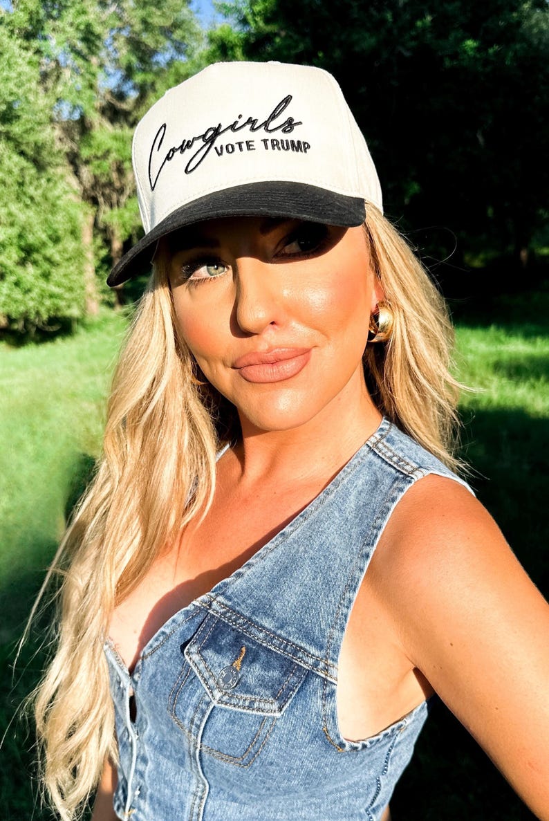 K&ouml;nnte beinhalten: Eine Frau tr&auml;gt eine wei&szlig;e und schwarze Baseballkappe mit dem Schriftzug "Cowgirls Vote Trump" in schwarzer Stickerei. Sie tr&auml;gt eine Jeansweste und hat blonde Haare.