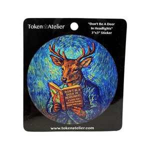 May include: A 3"x3" sticker featuring a deer-human hybrid reading a book titled "Don't Be A Deer In Headlights." The artwork has a blue and yellow color scheme with the text "Token Atelier" and "www.tokenatelier.com".