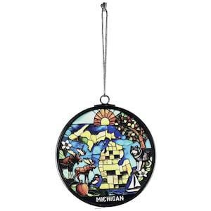 May include: Round stained glass ornament featuring a colorful depiction of the state of Michigan. The design includes a sunrise, map outline, moose, wolf, sailboat, and the word "MICHIGAN". The ornament is framed in black with a silver hanging chain.