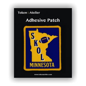 May include: Adhesive patch featuring a yellow outline of Minnesota with a blue interior. The patch includes a football graphic and the word "SKOL" and "MINNESOTA". The patch is bordered with yellow stitching and has the text "Token Atelier" at the top.