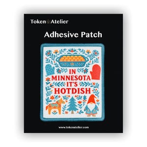 May include: Adhesive patch with a white background and a blue border. The patch features a colorful design with the text "IN MINNESOTA IT'S HOTDISH". The design includes a casserole dish, oven mitts, a Dala horse, a Christmas tree, and a gnome.