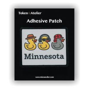 May include: Adhesive patch featuring three cartoon ducks, each with a different hat and sunglasses. The patch reads "Minnesota" in bold, black letters. The patch is on a black background, with the words "Token Atelier" and "Adhesive Patch" at the top.