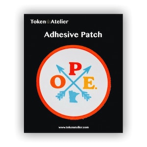 May include: Adhesive patch with a white circular design, featuring the word "OPE" in orange, red, and yellow, with blue arrows and a blue outline of Minnesota. The patch has an orange border and the text "Token Atelier" and "www.tokenatelier.com".