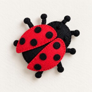 May include: A felt ladybug ornament featuring a solid black body and two bright red wings. The wings are decorated with six circular black felt spots. The insect has six small black legs extending from the sides of its round, textured body.