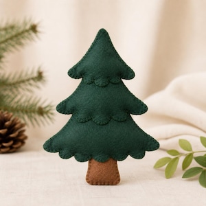 Puede incluir: Un adorno de árbol de Navidad de fieltro verde oscuro con tres niveles festoneados distintos y una base de tronco rectangular marrón. Los bordes del árbol están acabados con costuras visibles, creando una apariencia suave y en capas.