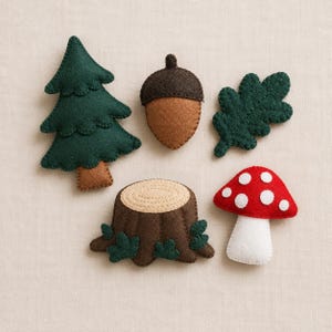May include: A collection of five felt ornaments featuring a dark green pine tree with a brown trunk, a brown acorn, a dark green oak leaf, a brown tree stump with small green leaves, and a red mushroom with white spots and a white stem.