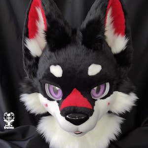 May include: Black and white furry wolf head with red ears and a red nose. The wolf has purple eyes and a white muzzle.