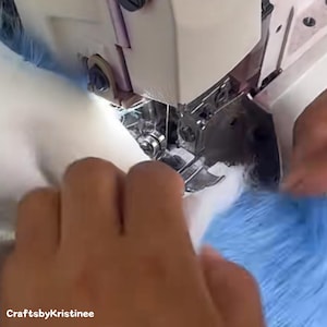 Peut inclure: Gros plan sur les mains d'une personne utilisant une machine &agrave; coudre pour coudre deux morceaux de tissu ensemble. Le tissu est blanc et bleu.