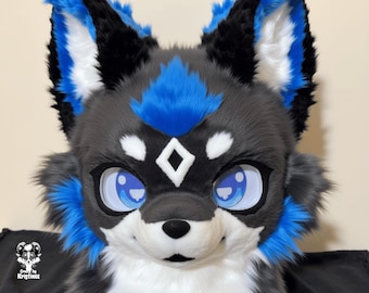 May include: A close-up of a furry wolf head with a diamond-shaped marking on the forehead. The head is primarily gray, with black and blue accents on the ears and around the eyes. The eyes are large and blue, and the nose is black.